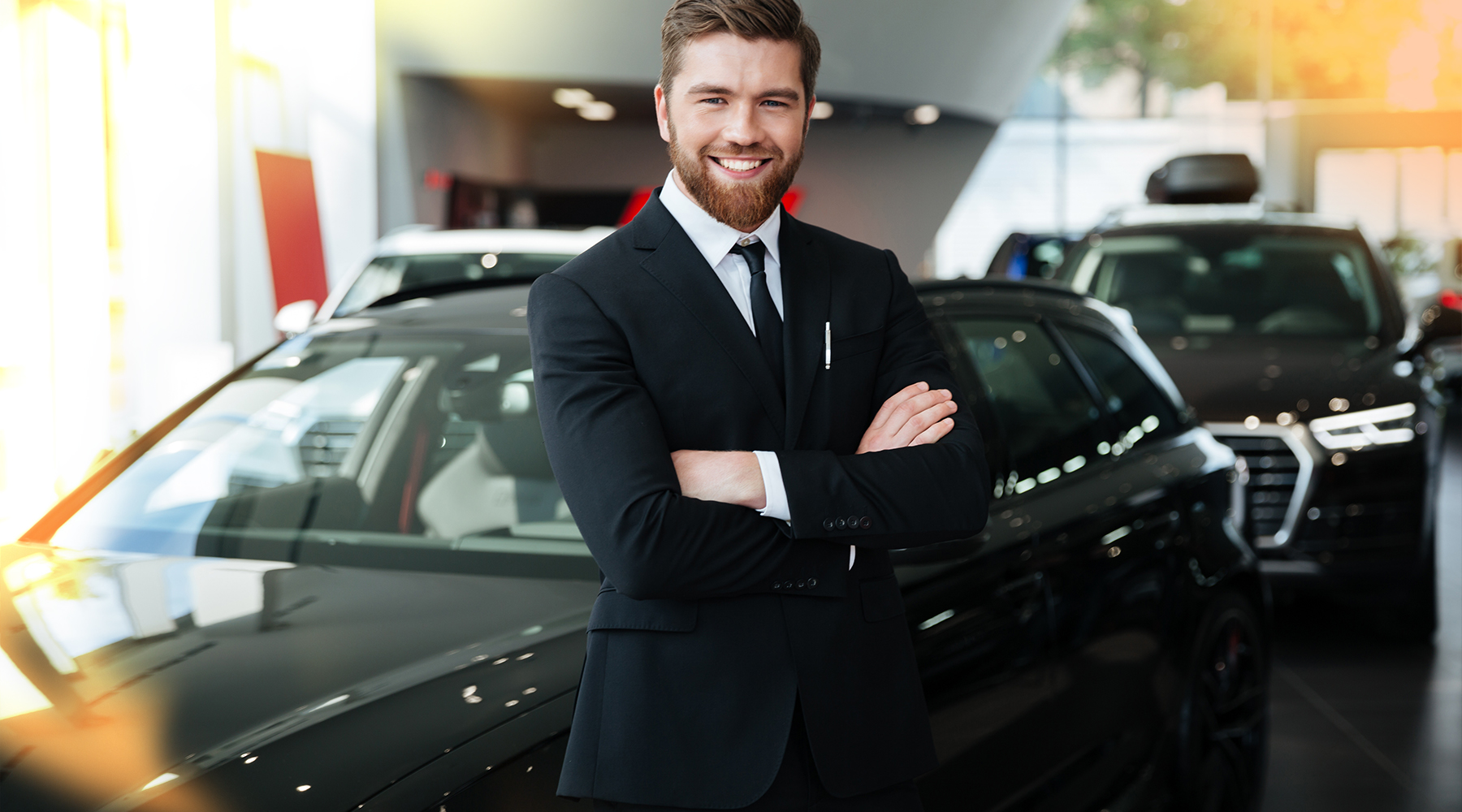 Automobilkaufmann Automobilkaufmann mit stabiler Pose und verschränkten Armen und einem lächeln in einer Autohaus.