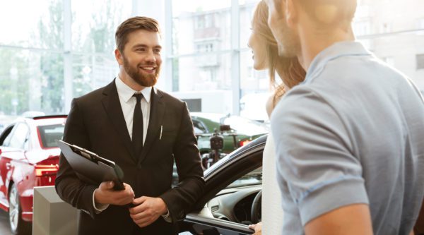 Ein Automobilkaufmann Verhandelt mit einer Kundin und einem Kunden in einer Autogalerie.