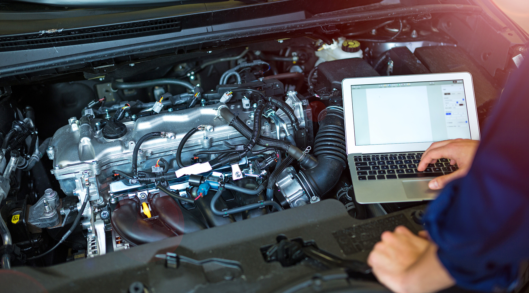 Diagnosetechniker an einer offenen Motorhaube eines Fahrzeuges nimmt Messungen vor.