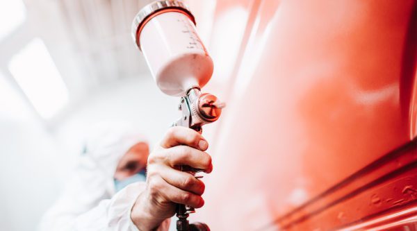 Mann Lackiert im Lackierraum ein Auto in Rot.