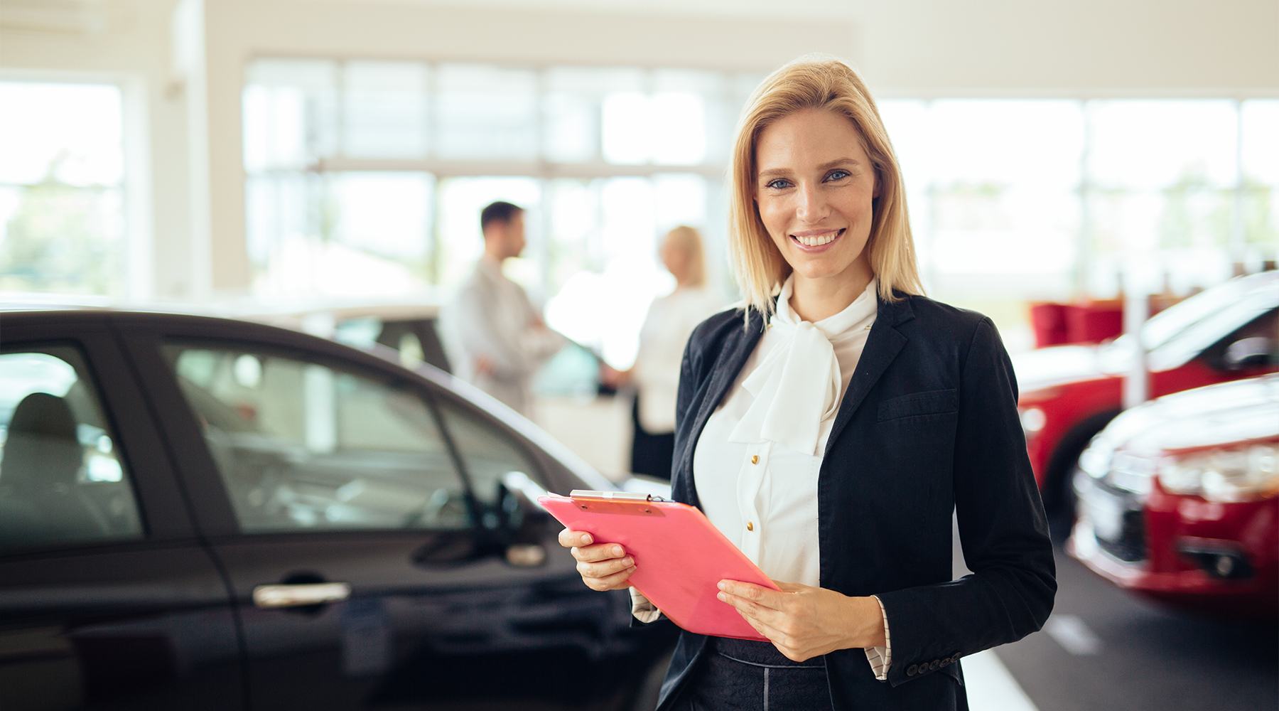 Filialleiterin im Autohaus mit einem Dokument in der Hand. Im Hintergrund sind zwei Personen zu sehen.