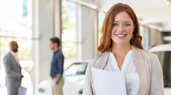 Serviceassistentin im Autohaus. Im Hintergrund zwei unterhaltende Herren