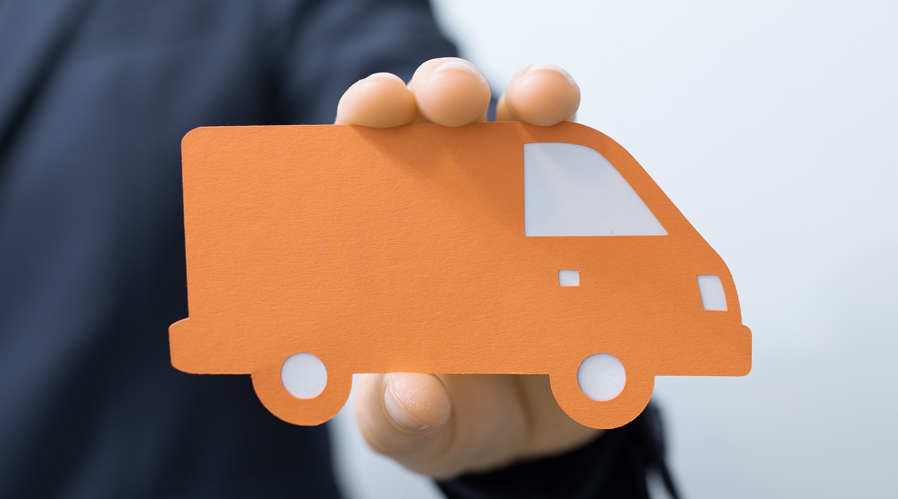Verkaufsberater für Nutzfahrzeuge Verkaufsberater für Nutzfahrzeuge hält einen in Papier zurechtgeschnittenen Transporter in orangener Farbe in der Hand.
