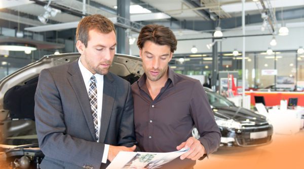 Verkaufsberater für Neuwagen beratend mit einem Kunden in einer Autogalerie.