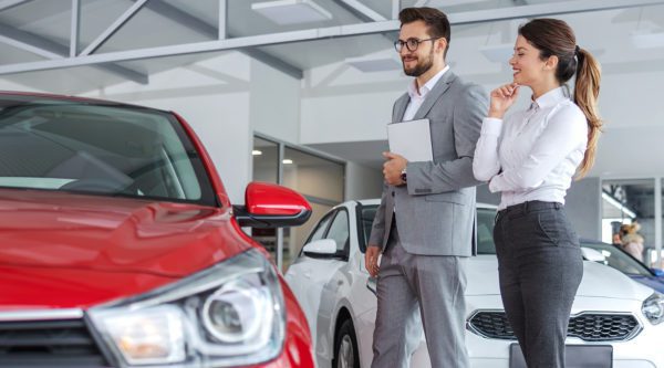 Verkaufsberater Gebrauchtwagen mit Kundin in einer Autogalerie