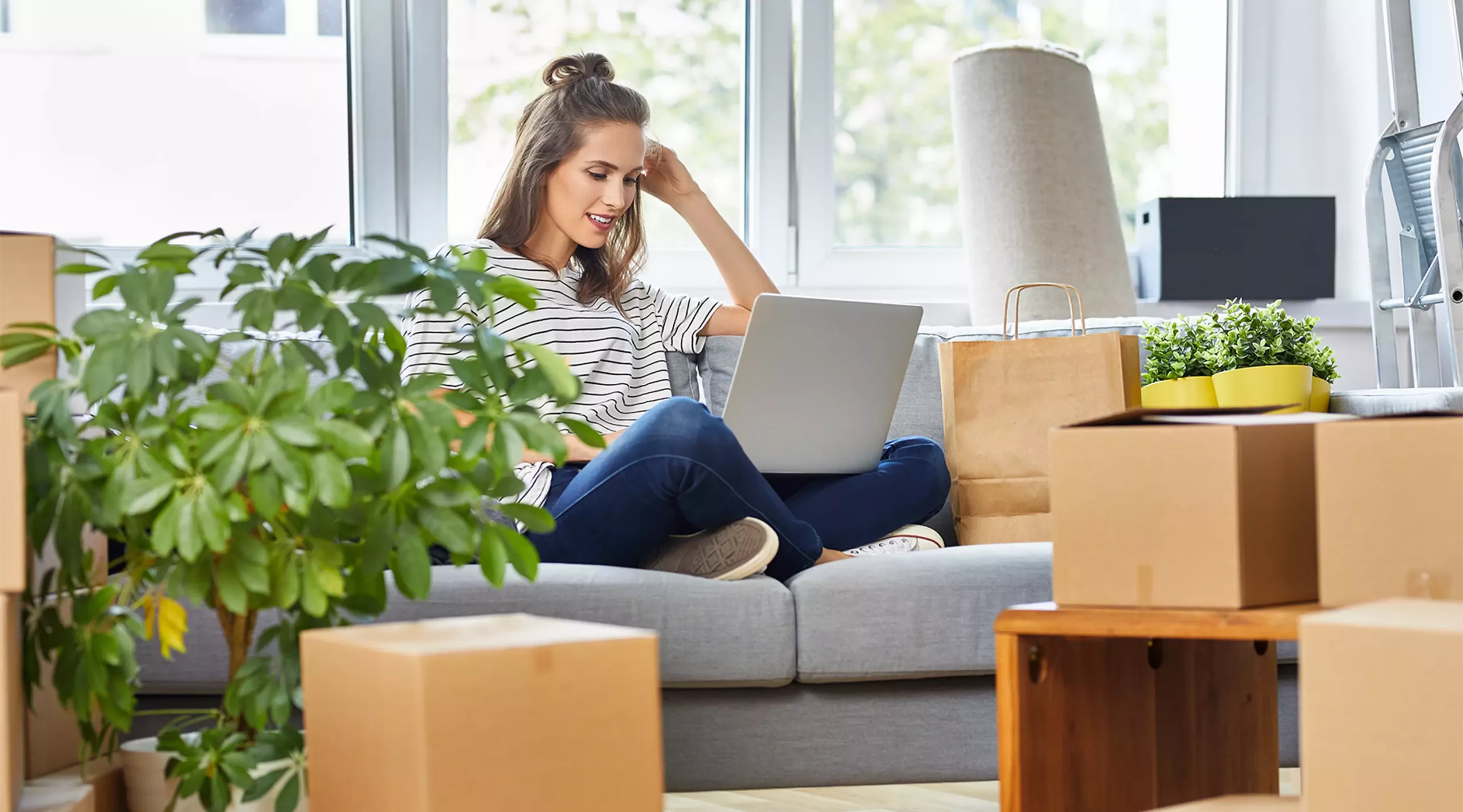 Junge Frau sitzt auf dem Sofa mit Laptop beim Einzug in eine neue Wohnung Junge Frau sitzt auf dem Sofa mit Laptop beim Einzug in eine neue Wohnung